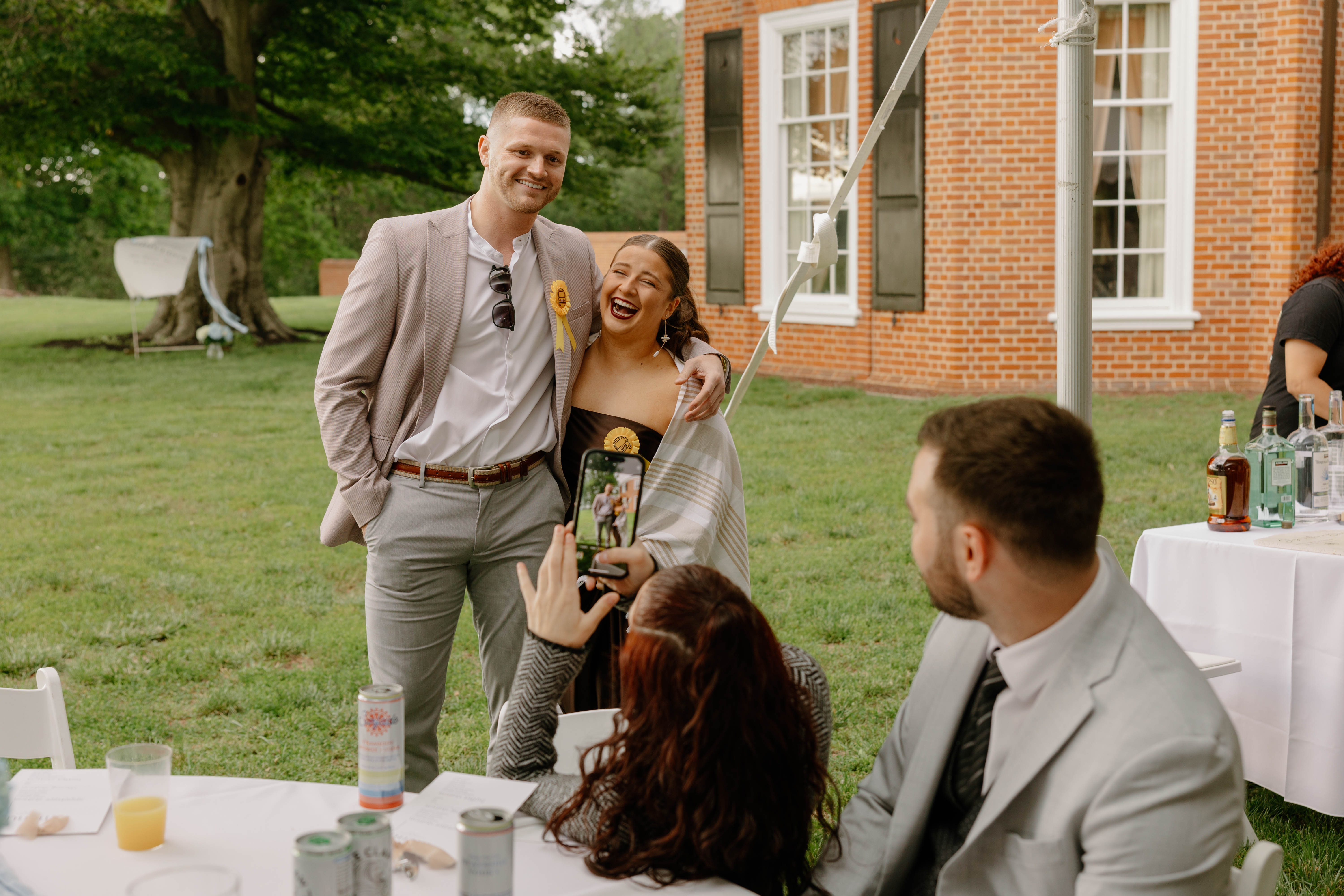 Two guests embracing and smiling while another guests takes a photo of them.